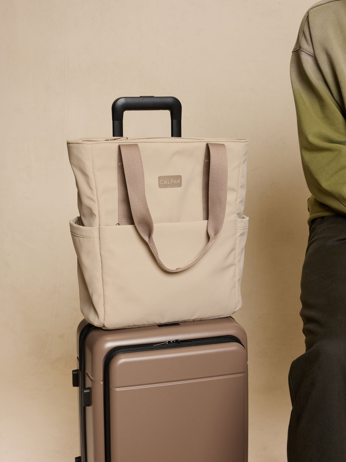 CALPAK Zippered Laptop Tote Bag in beige Greige on a suitcase against a beige background; TCN2501-GREIGE
