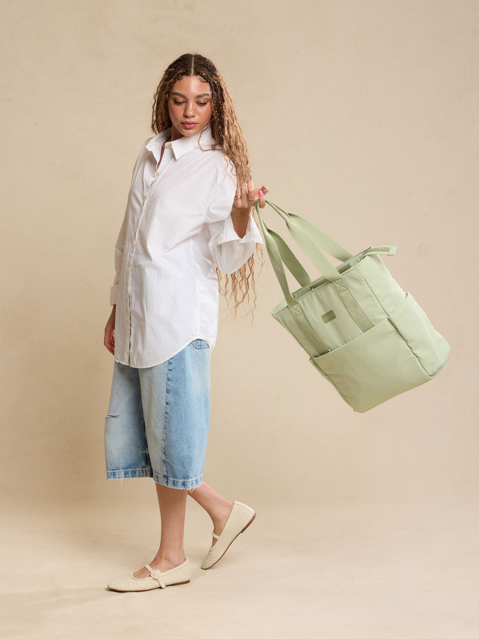 CALPAK Zippered Laptop Tote Bag in light green Meadow on a beige background being held by a model; TCN2501-MEADOW