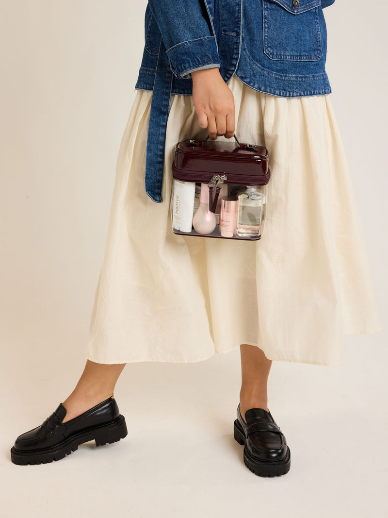Model carrying the CALPAK Clear Train Case in maroon Glazed Dark Cherry