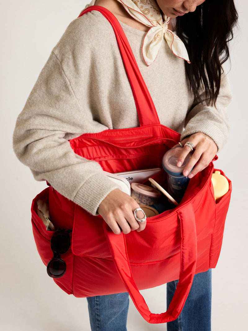 Woman adding items into CALPAK Diaper Tote bag in red Tomato
