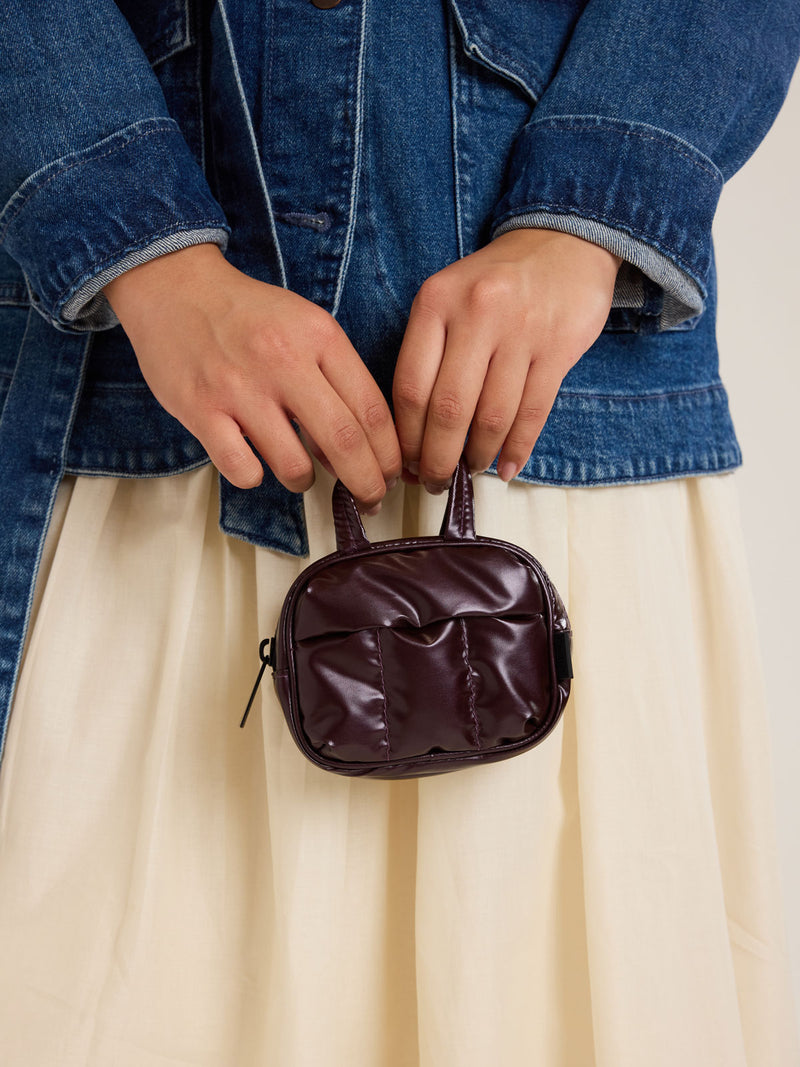 Model holding CALPAK Luka Duffel Key Pouch in maroon Glazed Dark Cherry on a white background