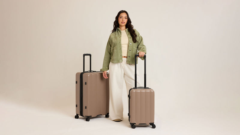 Woman with the CALPAK Evry Starter Bundle in brown Chocolate with the Carry On and Large sizes