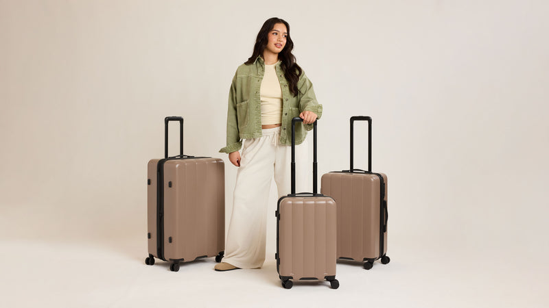 Woman standing with Carry-On, Medium, and Large Evry luggage in brown Chocolate