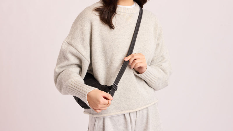 Person with a grey sweater wearing the CALPAK Luka Crescent Bag in Black as a crossbody 