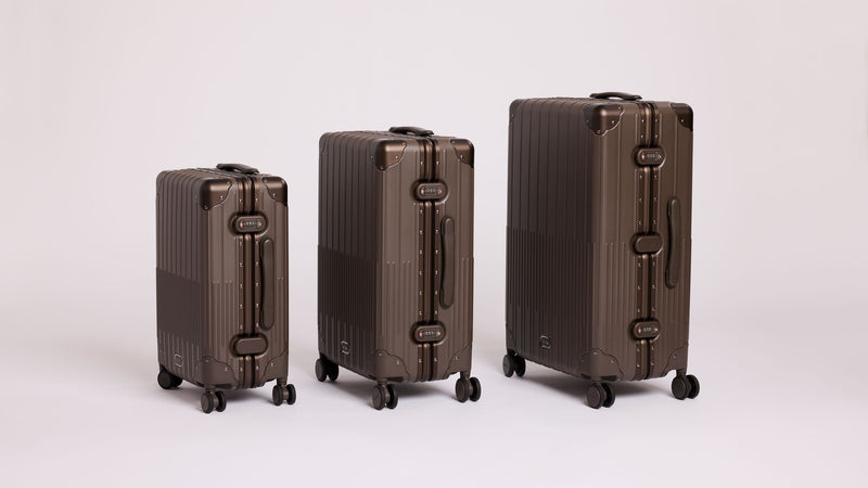 Three hard-shell aluminum framed CALPAK Vault Luggage suitcases arranged by size from left to right on a seamless light gray studio background.