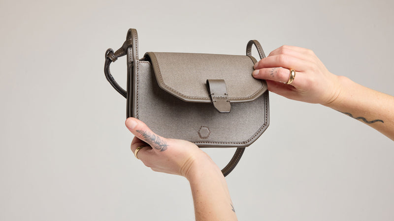Person holding a small gray Colette Canvas Crossbody Wallet bag against a plain background