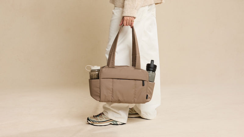 CALPAK Luka Mini Duffel shown with two water bottles in exterior pockets