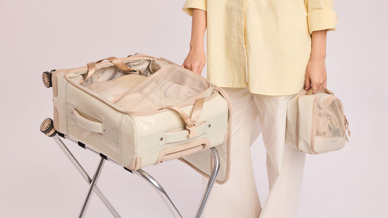 Person packing a suitcase with the CALPAK Terra 5pc Packing Cubes in off white beige White Sands color on a light background