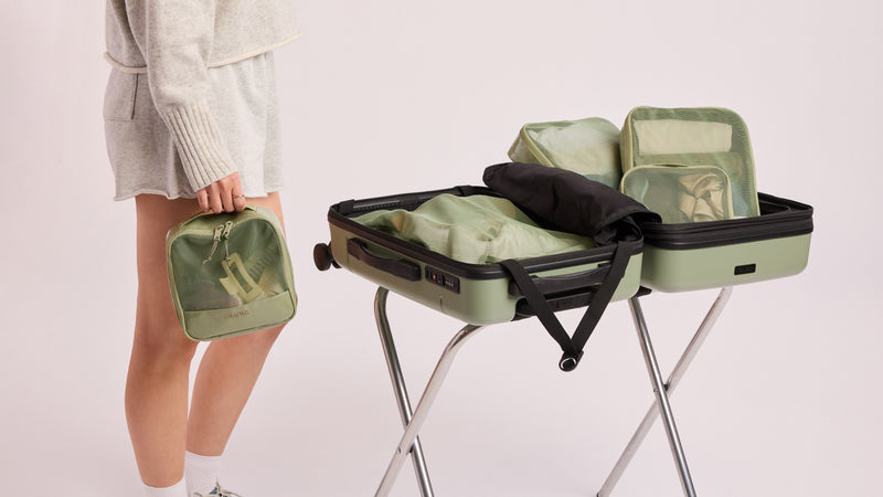 Person packing a suitcase with the CALPAK Terra 5pc Packing Cubes in olive green Juniper color on a light background