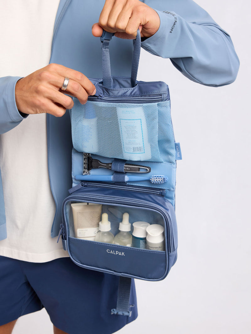 Model holding open the CALPAK Fit Hanging Dopp Kit in blue Indigo