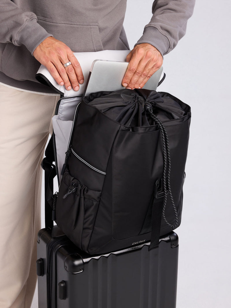 Model using trolley sleeve feature of CALPAK Fit Gym Backpack in Black front view with white background