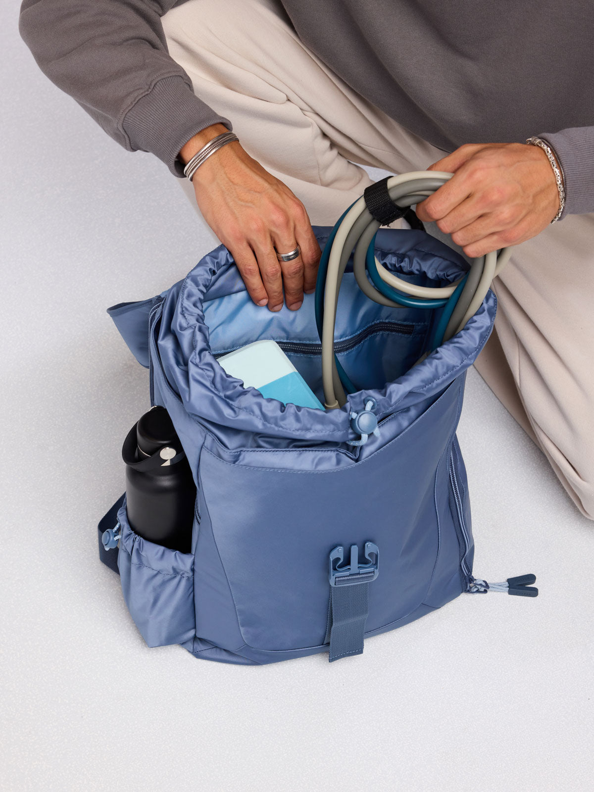 Person adding gym essentials to the CALPAK Fit Gym Backpack in blue Indigo; BPF2601-INDIGO
