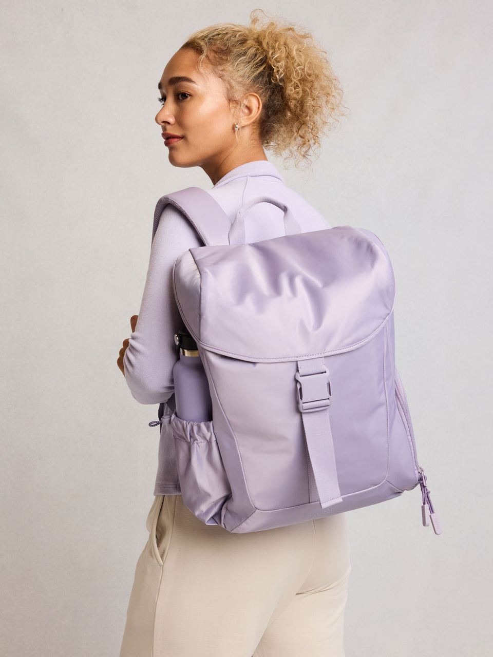 Model wearing CALPAK Fit Gym Backpack in light purple Iris front view with white background; BPF2601-IRIS