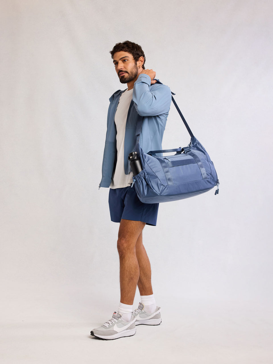 Man wearing CALPAK Fit Gym Duffel Bag in blue  Indigo; TBF2401-INDIGO
