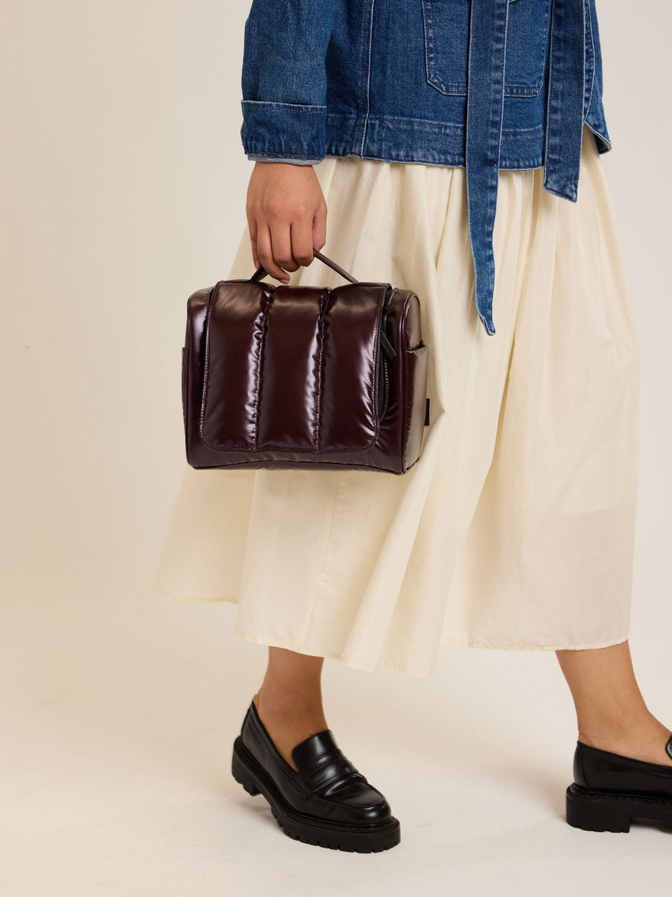 Model carrying the CALPAK Luka Hanging Toiletry Bag in maroon Glazed Dark Cherry; TLH2301-GLAZED-DARK-CHERRY
