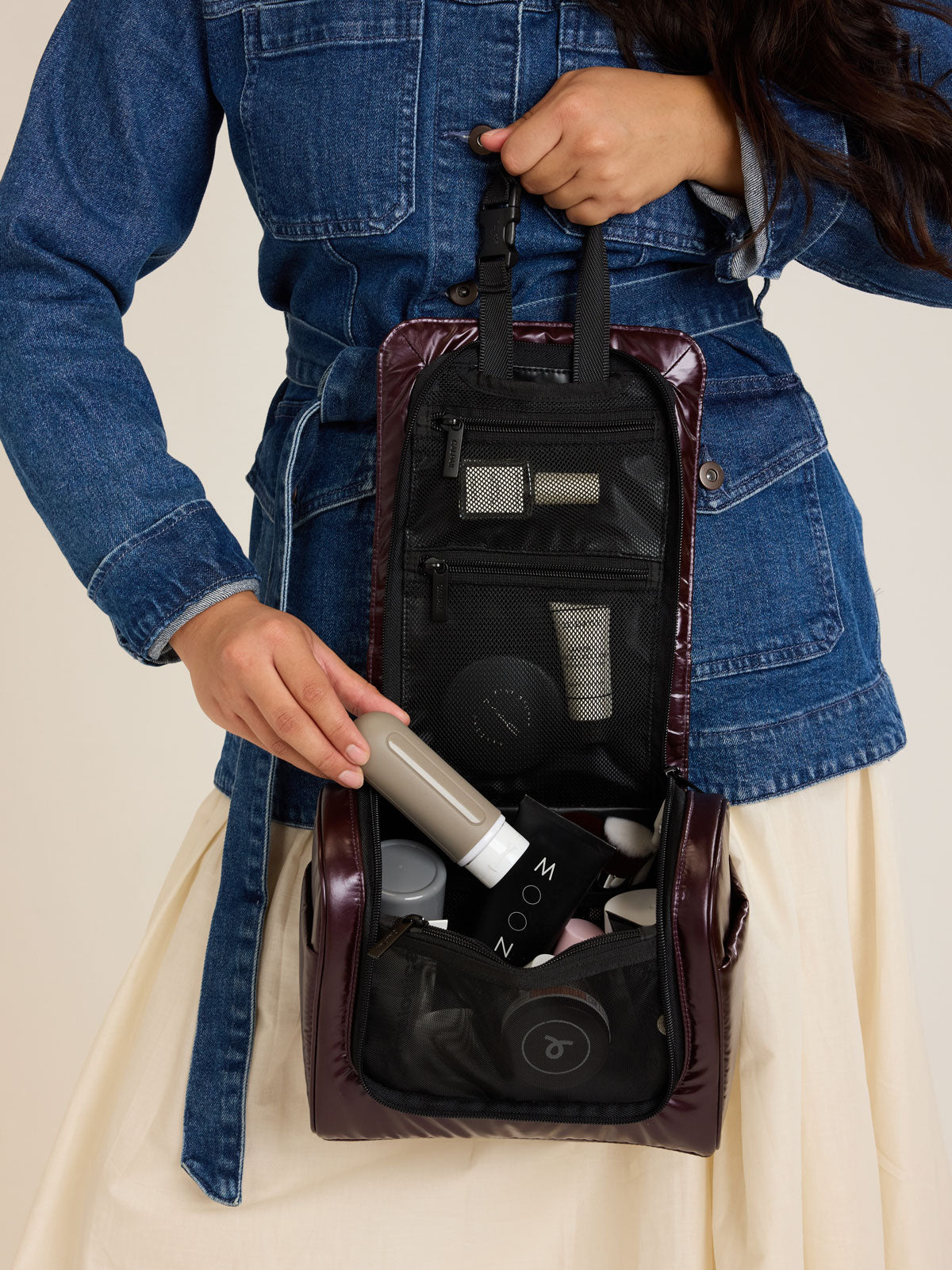 Model packing the CALPAK Luka Hanging Toiletry Bag in maroon Glazed Dark Cherry; TLH2301-GLAZED-DARK-CHERRY