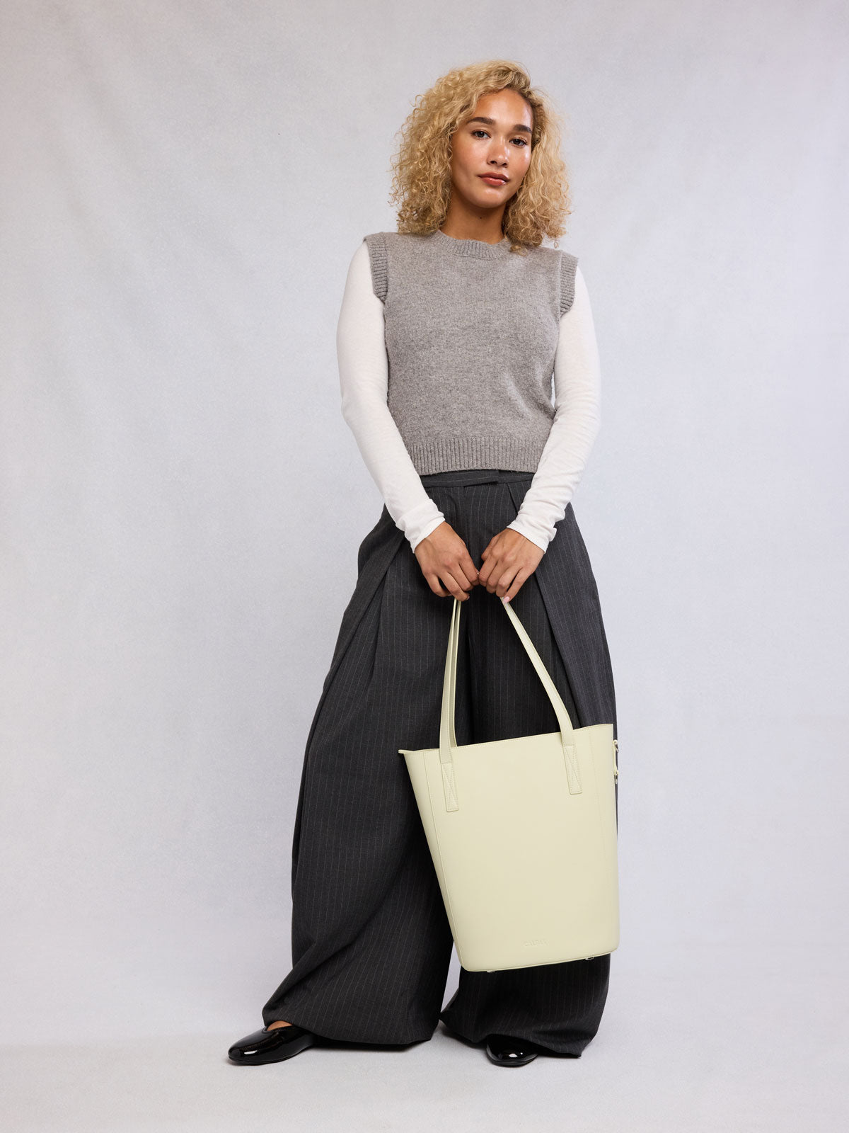 Woman holding the CALPAK Haven 14" Haven Laptop Tote in light green Celadon; ABU2501-CELADON