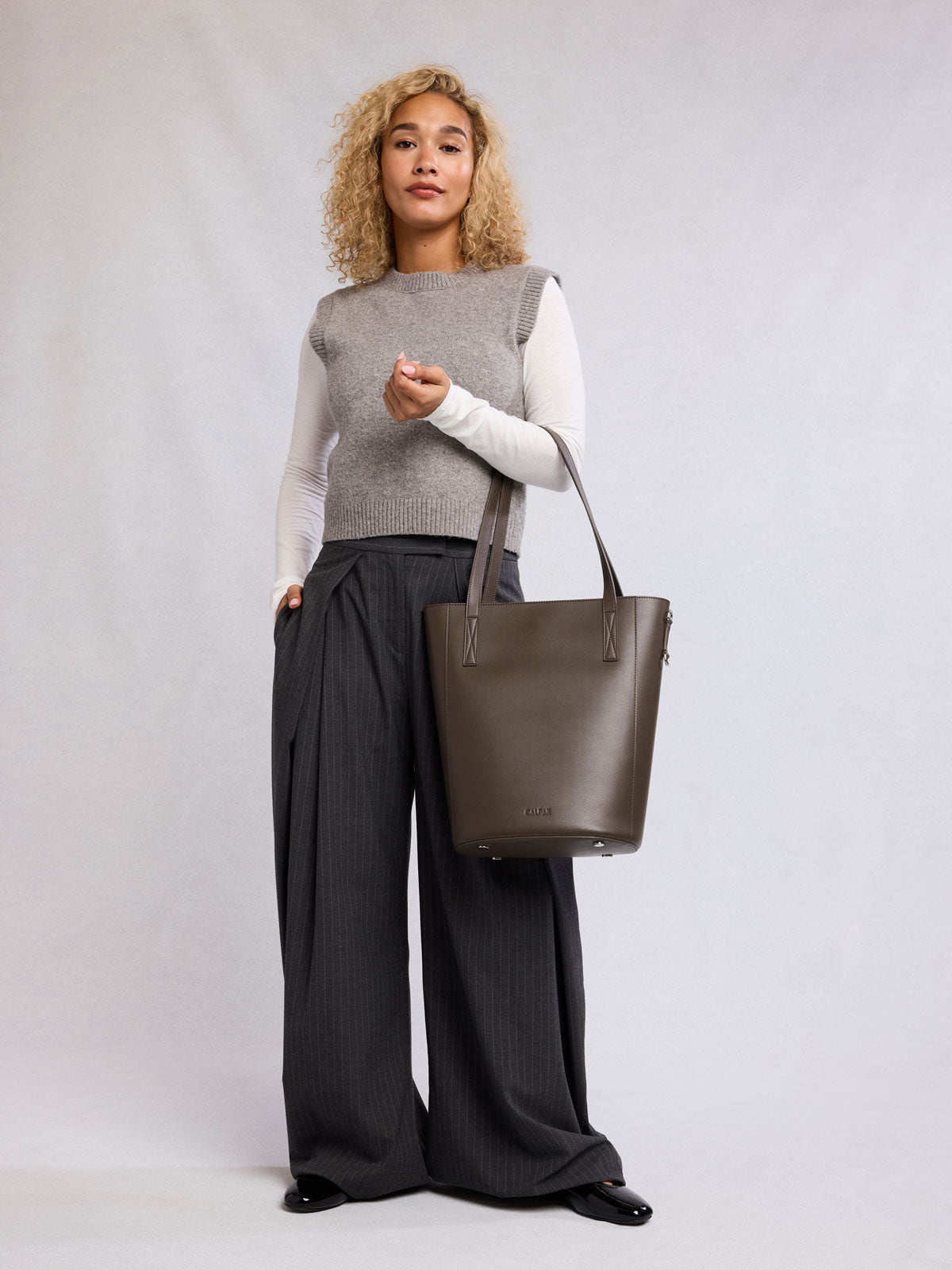 Woman holding the CALPAK Haven 14" Haven Laptop Tote in dark brown Mushroom; ABU2501-MUSHROOM
