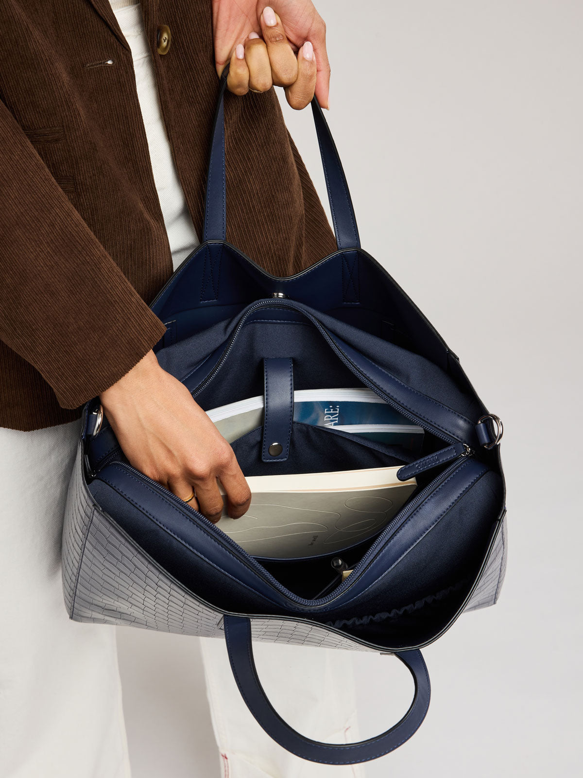 A navy blue croc-embossed tote bag with a gray plaid patterned body, shown being held by a person wearing a brown corduroy jacket; ATO2102-NAVY-FAUX-CROC