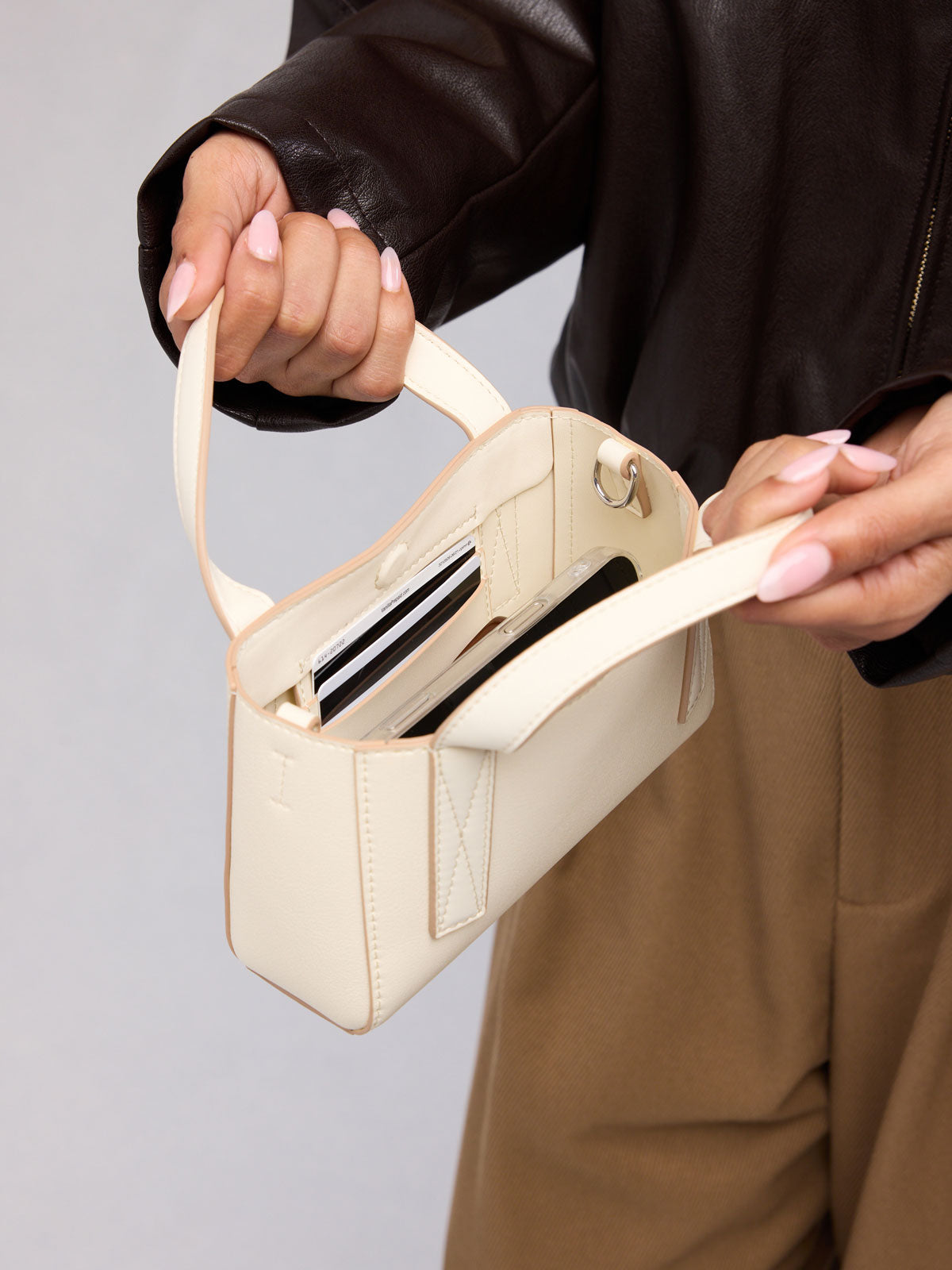 Person holding open the CALPAK Haven Mini Crossbody Bag in beige Buttercream; AMC2501-BUTTERCREAM