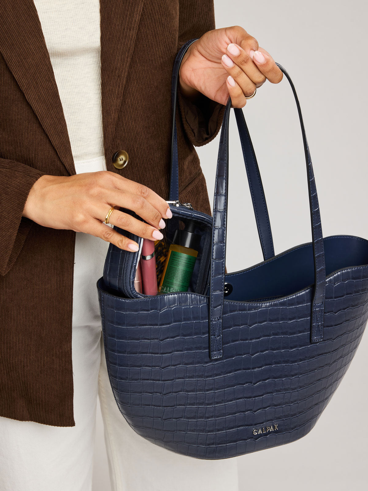 A Haven Tulip Tote in Navy blue crocodile-embossed with dual shoulder straps, held by a person wearing a brown blazer and white pants; AHP2601-NAVY-FAUX-CROC