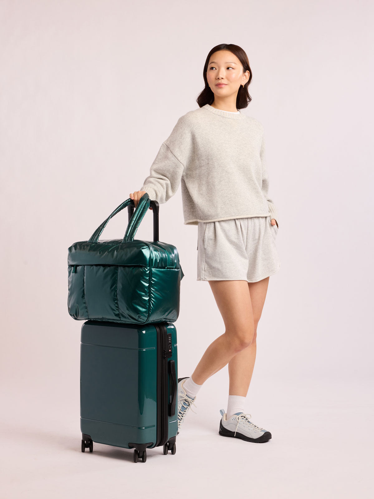 Woman with CALPAK Luka Duffel with the Hue Carry On Luggage both in dark green shiny Glazed Kale; CALPAK Hue Carry On Luggage in dark green Glazed Kale; LHU1020-NP-GLAZED-KALE