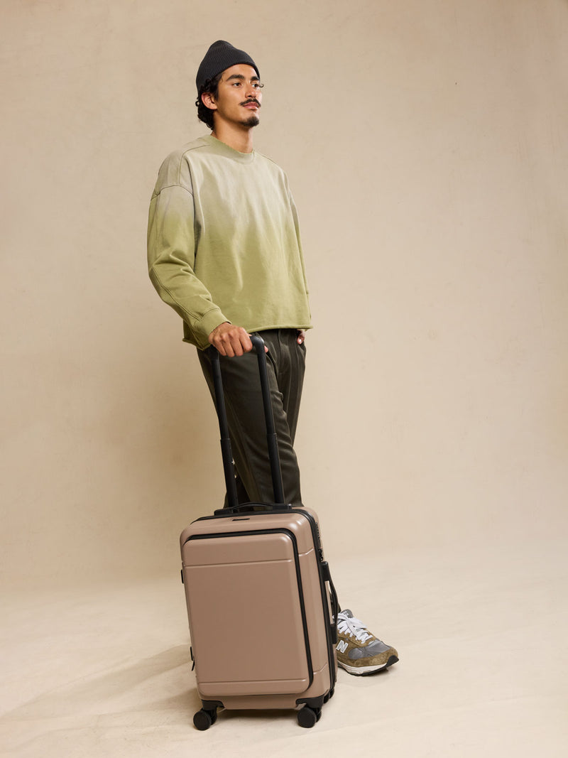 Model holding CALPAK Hue Front Pocket Carry On Luggage front view in brown Chocolate