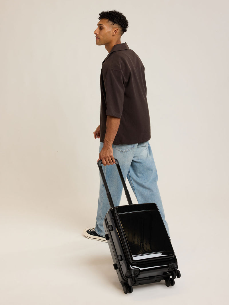 Model rolling the CALPAK Hue Front Pocket Carry On Luggage in Glazed Black
