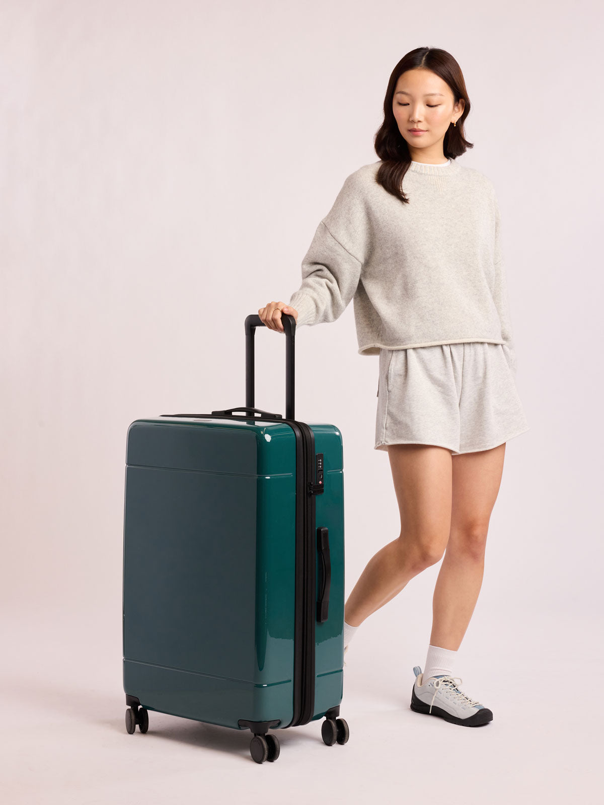 Woman with CALPAK Hue Large Luggage in dark green Kale; LHU1028-GLAZED-KALE
