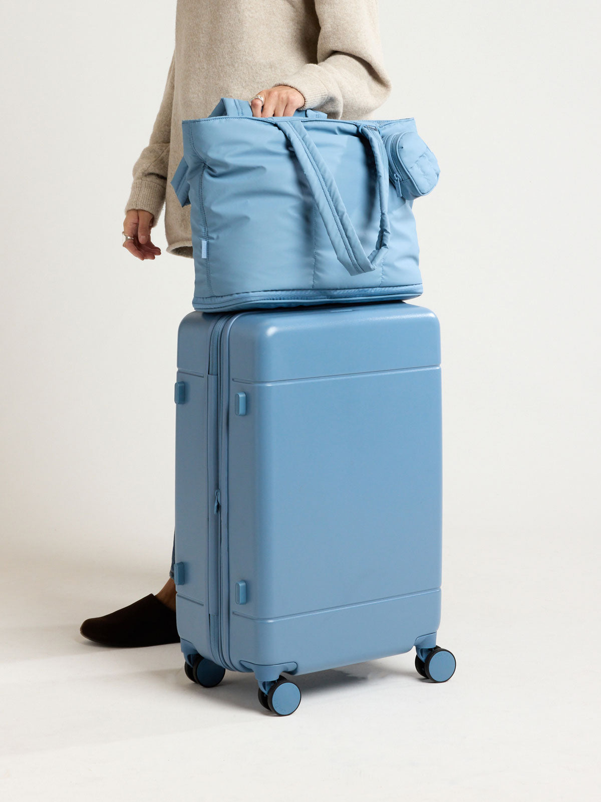 Model with CALPAK Hue Medium Luggage in light blue French Blue and blue and white gingham interior ; LHU1024-FRENCH-BLUE