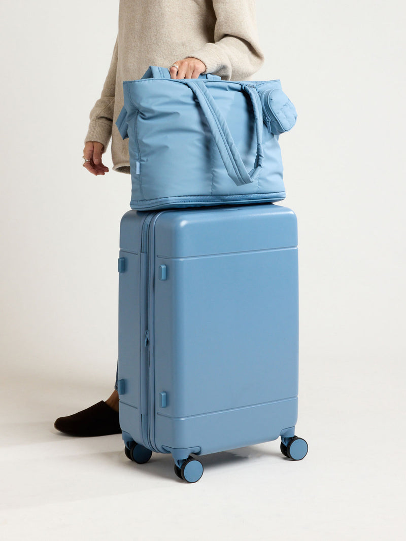 Model with CALPAK Hue Medium Luggage in light blue French Blue and blue and white gingham interior