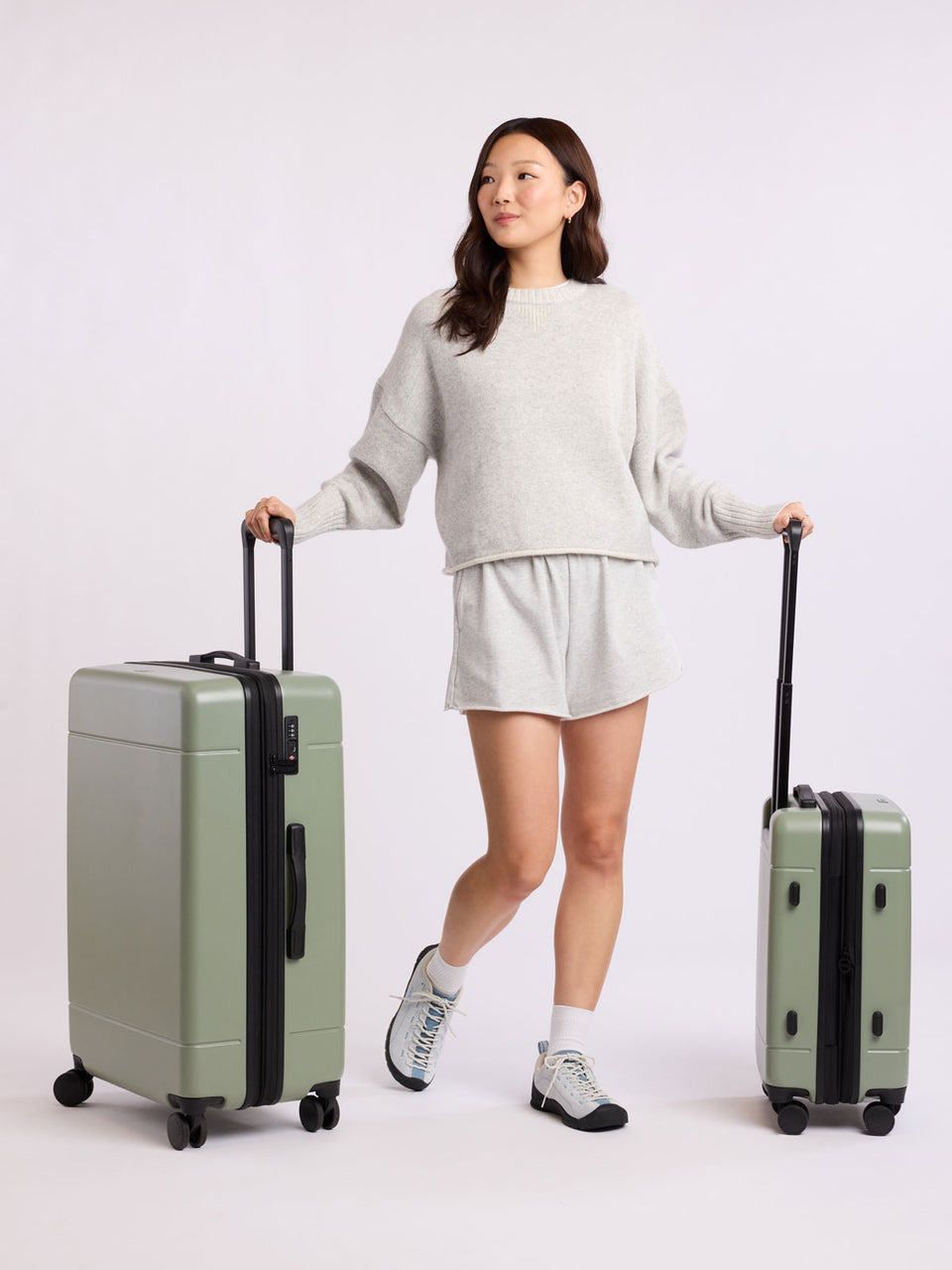 Woman holding two green CALPAK luggage part of Hue Starter Bundle on a white background; LHU8000-JUNIPER