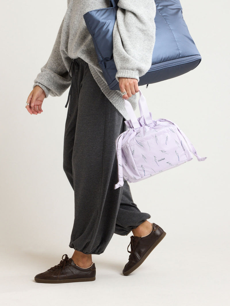 Model holding the CALKPAK Insulated Lunch Bag in lavender purple with lavender flower print