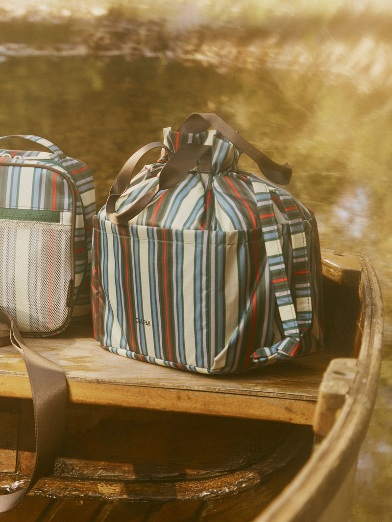 CALPAK Insulated Lunch Bag in multicolor (celadon, mushroom, french blue, lavender) striped Riviera Stripe on a bench