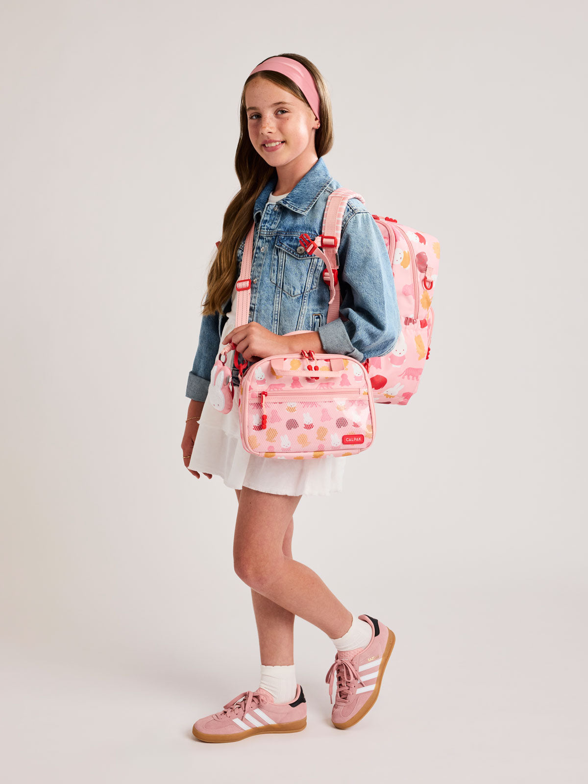 Girl with a CALPAK Kids Large Backpack with Miffy and pink colorful animal pattern on a white background; CKBL2501-MIFFY-PINK-ZOO-TRIP