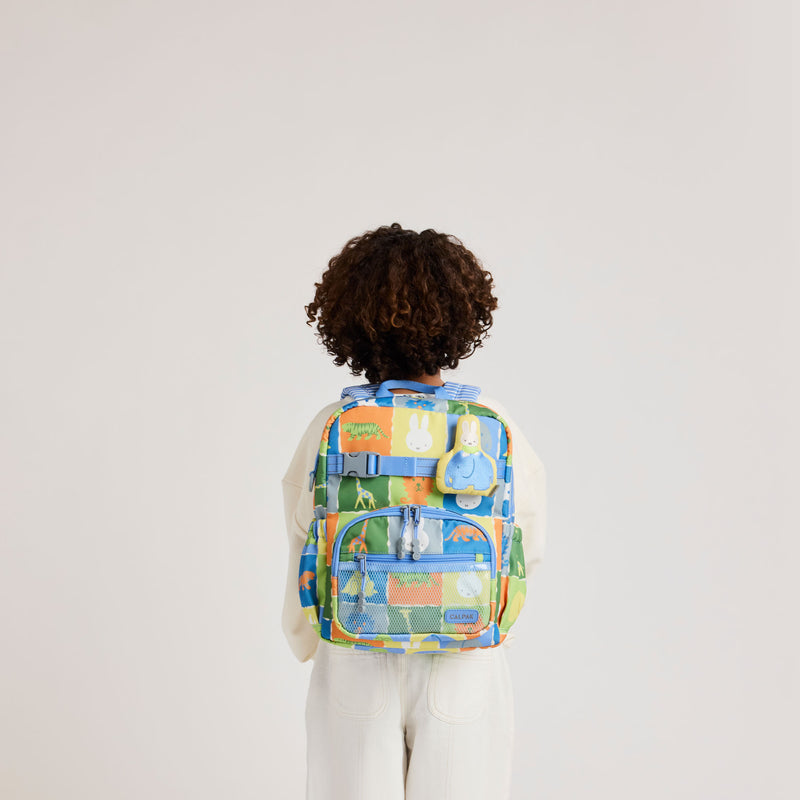 Child wearing the CALPAK + Miffy Small Backpack in Miffy Blue Zoo Trip featuring Miffy and other animal characters with colorful tiles
