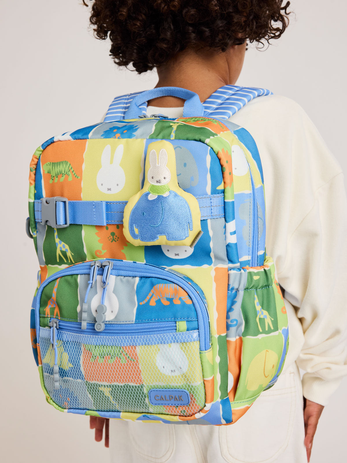 Child wearing Plush Miffy x CALPAK Pluffy Bag Charm keychain with a yellow border and Miffy on a blue elephant attached to a color Kids CALPAK Kids Backpack; APLF2501-MIFFY-ELEPHANT