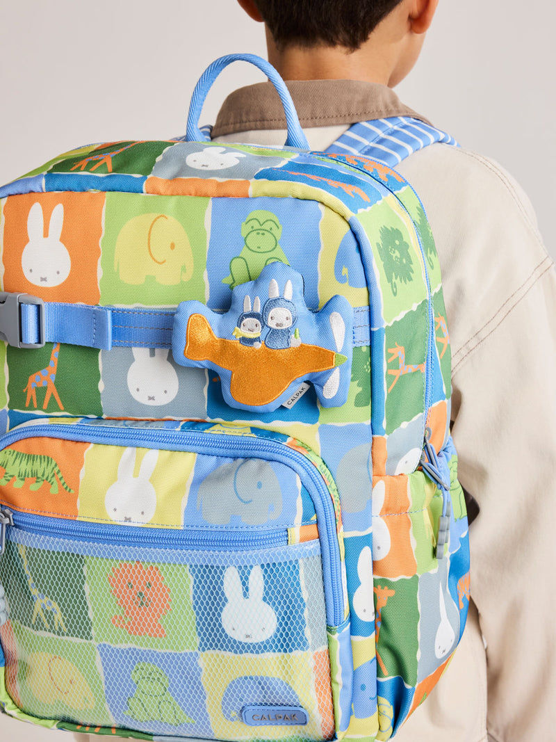 Child wearing Miffy x CALPAK Pluffy Bag Charm keychain with a blue border and Miffys holding a carrot on an orange airplane attached to a color Kids CALPAK Kids Backpack