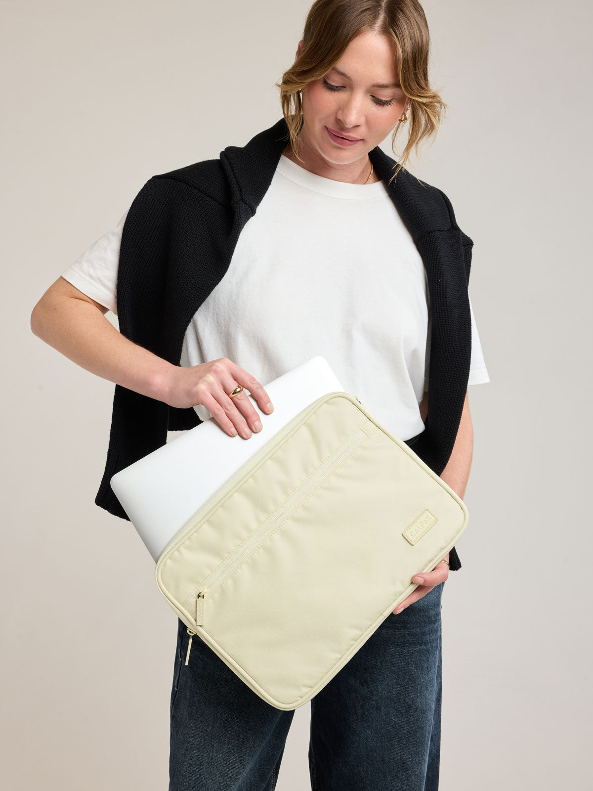 Woman putting laptop into CALPAK Padded Laptop Sleeve 13-14" in light green Celadon; ALP2213-CELADON