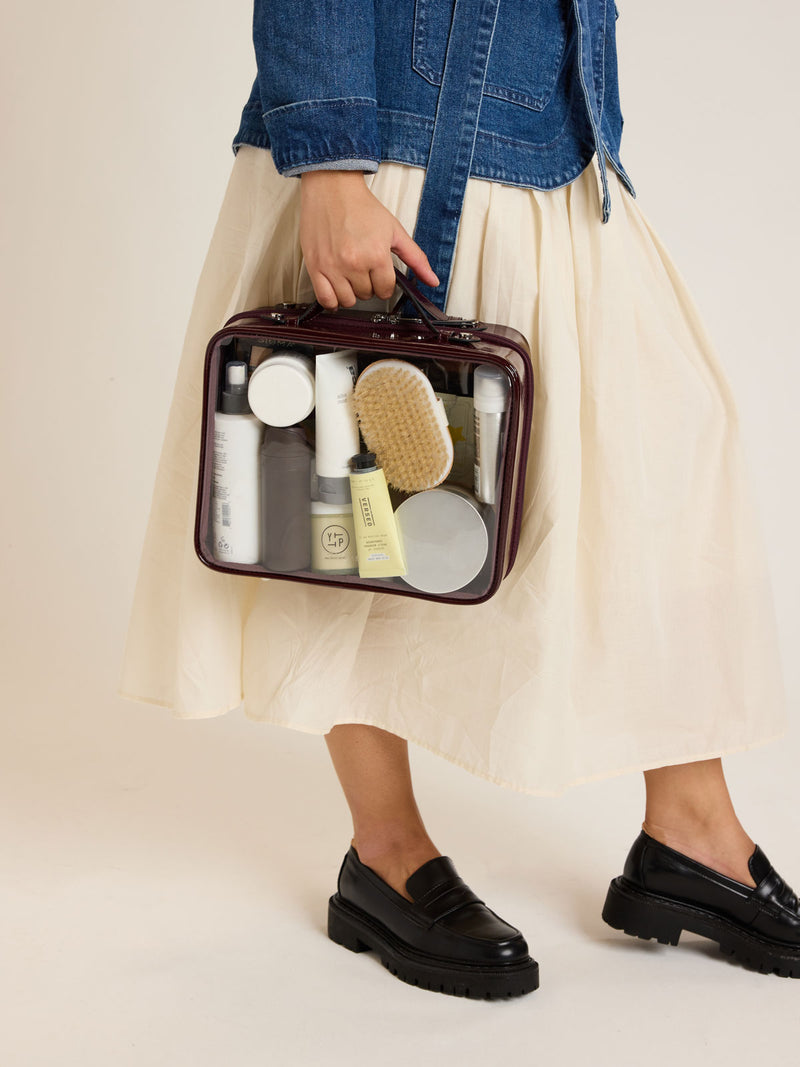 Model holding the CALPAK Large Clear Cosmetics Case in maroon Glazed Dark Cherry