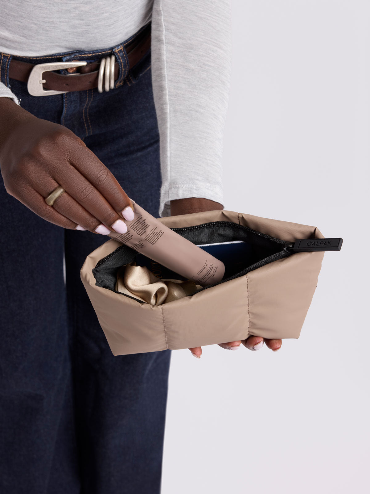 A close-up of a person holding a CALPAK Luka 1QT Zip Pouch in brown Chocolate; ZLPS2601-CHOCOLATE