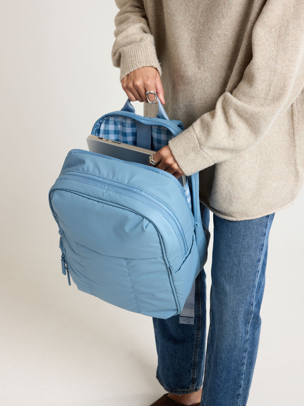 Person adding a laptop into the CALPAK Luka 15" Backpack in light blue French Blue; BPL2001-FRENCH-BLUE