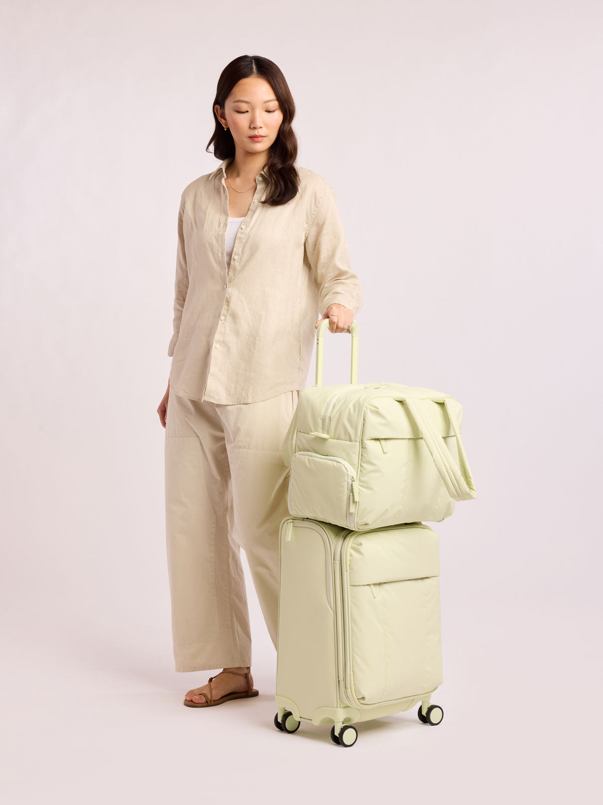 Model with CALPAK Luka Soft-Sided Carry On Luggage in light green Celadon on a white background with handle and spinner wheels; LSM1020-CELADON