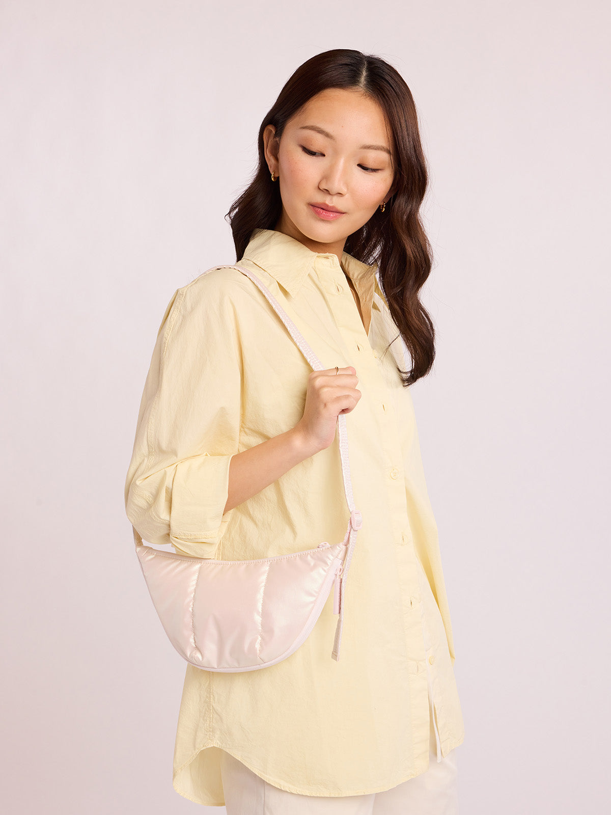 Woman with CALPAK Luka Crescent Bag in light pink shiny Pearlescent; CBL2601-PEARLESCENT