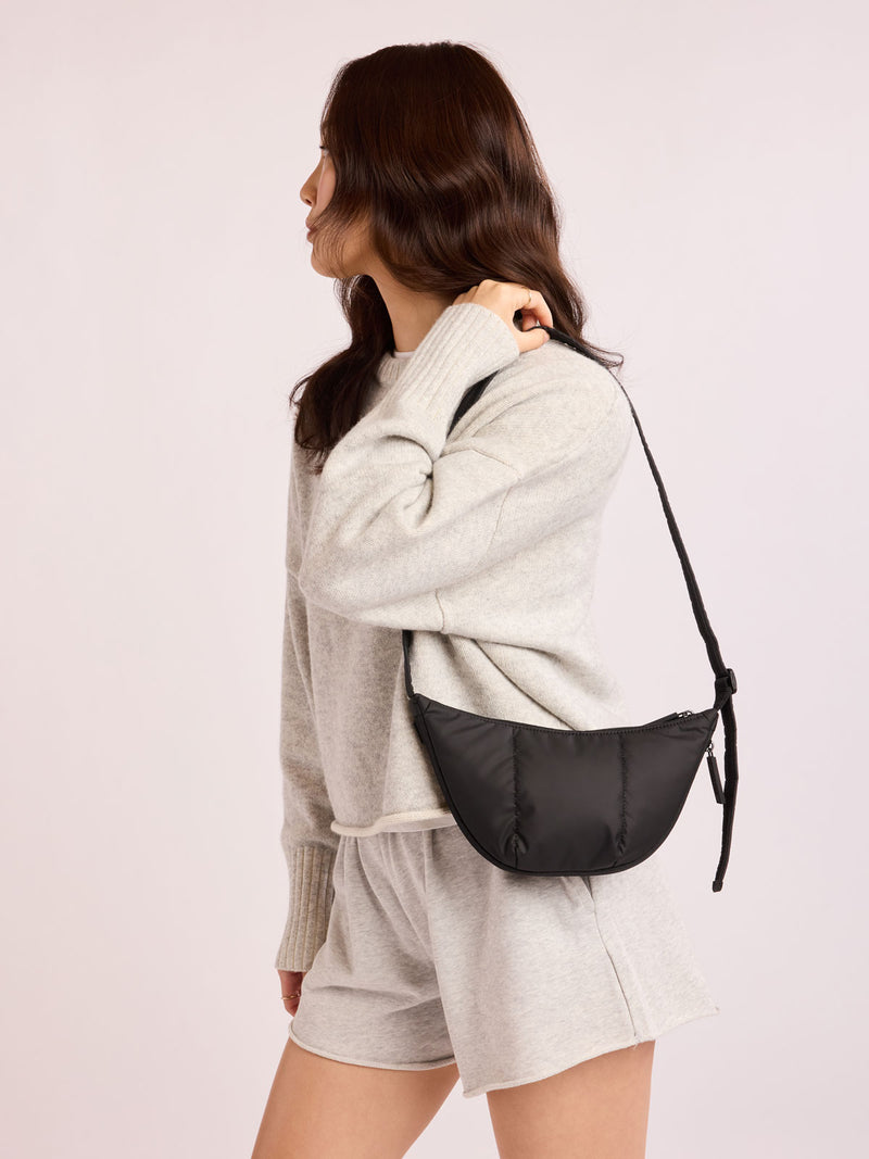 Model with grey outfit wearing CALPAK Luka Crescent Bag in Black