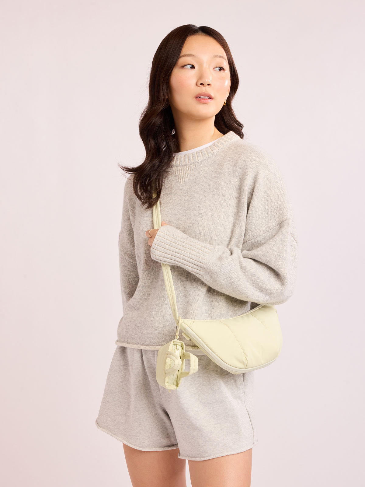 Model in grey outfit wearing the CALPAK Luka Crescent Tote bag in light green Celadon with shoulder strap and bag is expandable up to 2" on a white background; CBL2601-CELADON