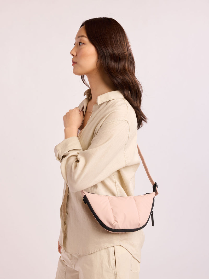 Model in beige outfit wearing CALPAK Luka Crescent Bag in light pink Rose Quartz