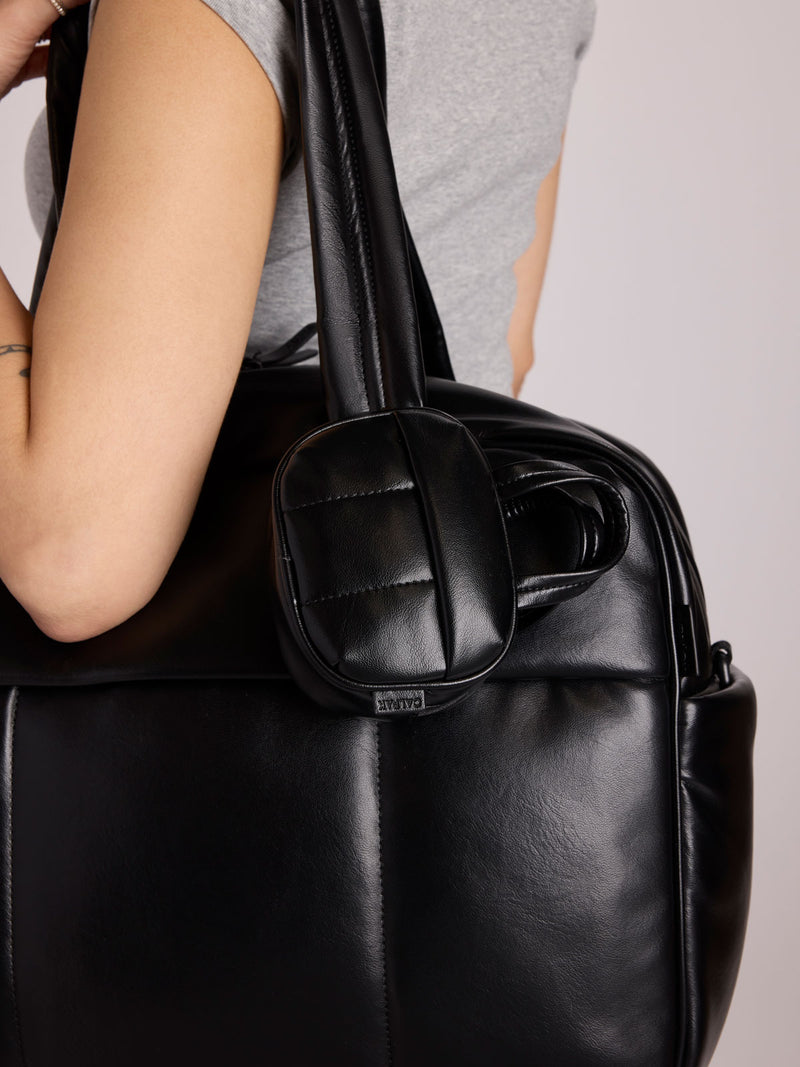 A close-up of a person carrying a CALPAK Luka Duffel in Vegan Leather with a matching CALPAK Luka Duffel Zip Bag Charm attached to the shoulder strap