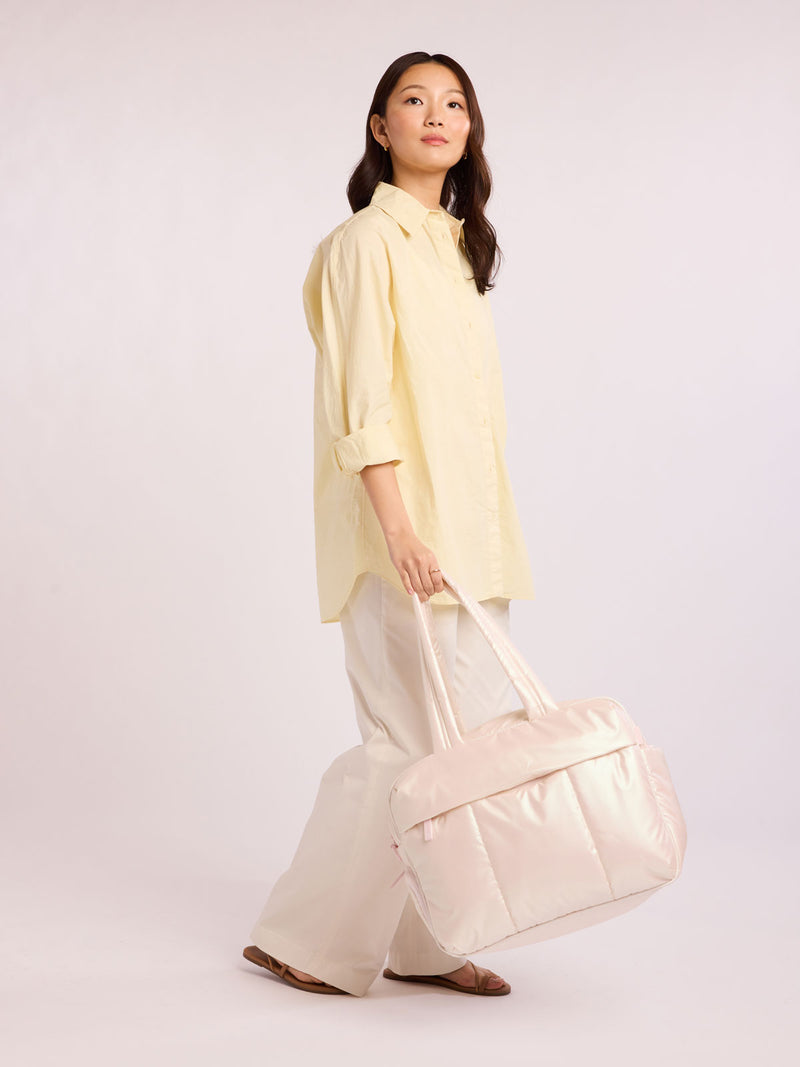 Woman holding CALPAK Luka Duffel in light pink shiny Pearlescent
