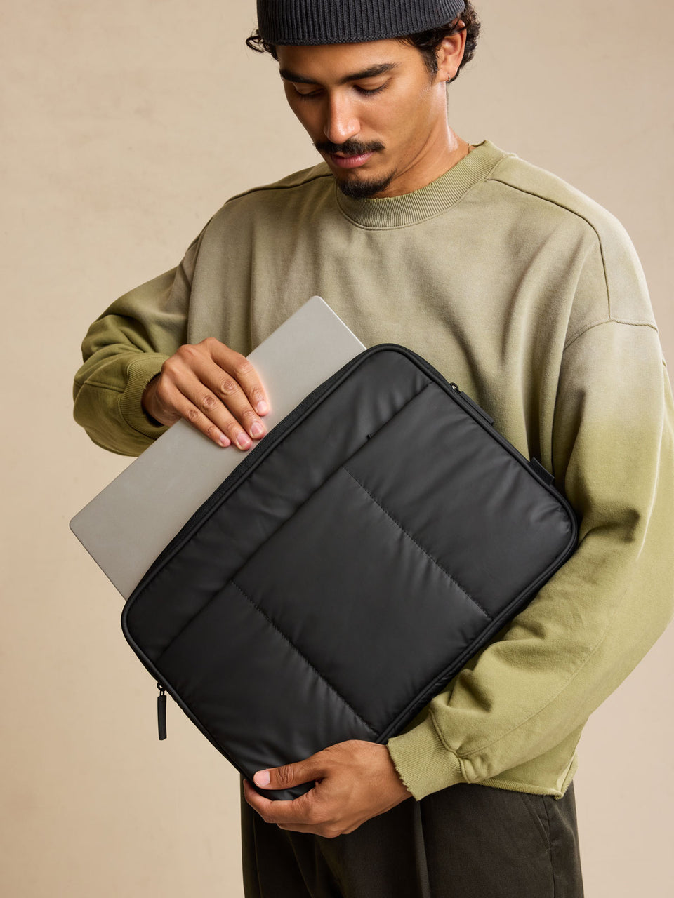 Model putting in laptop into CALPAK Luka 17-in Padded Laptop Sleeve in black Matte Black with puffy exterior; ALD2501-MATTE-BLACK